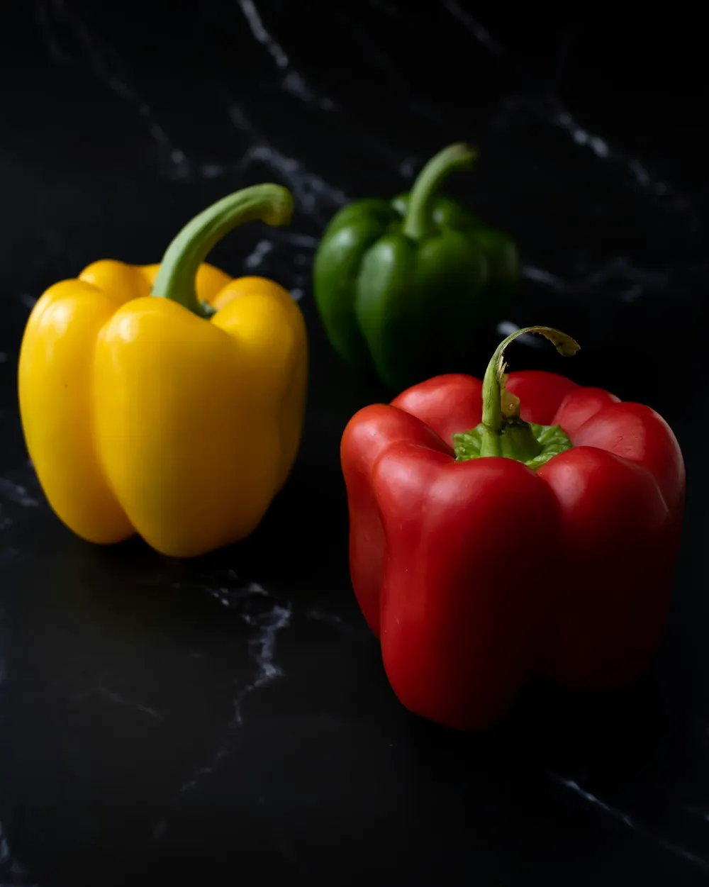 Red, yellow and green capsicums on a dark marble bench