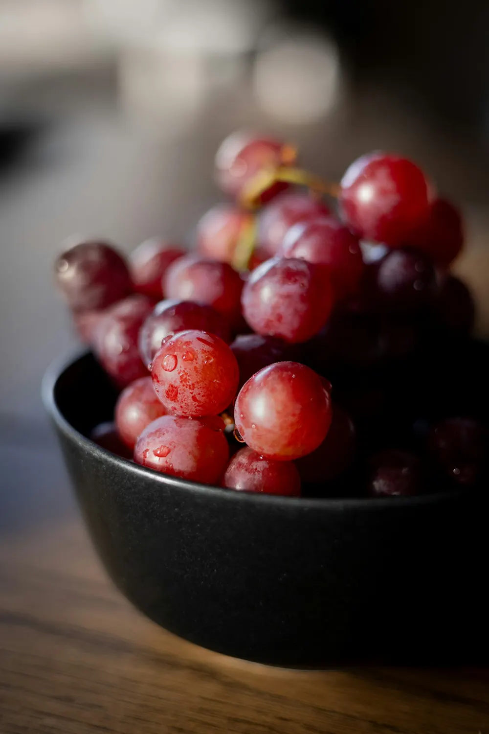 Red table grapes piled in a dark bowl on a wooden bench